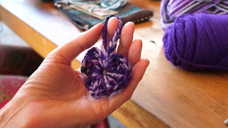 Close up of a crocheted heart being held by a woman's fingers.