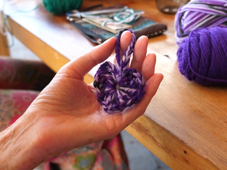 Close up of a crocheted heart being held by a woman's fingers.