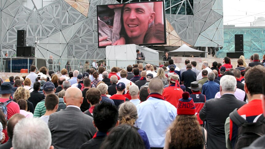 People at Federation Square in Melbourne watch Jim Stynes state funeral.