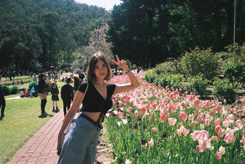 A young woman smiling and posing by a colourful flowerbed on a sunny day