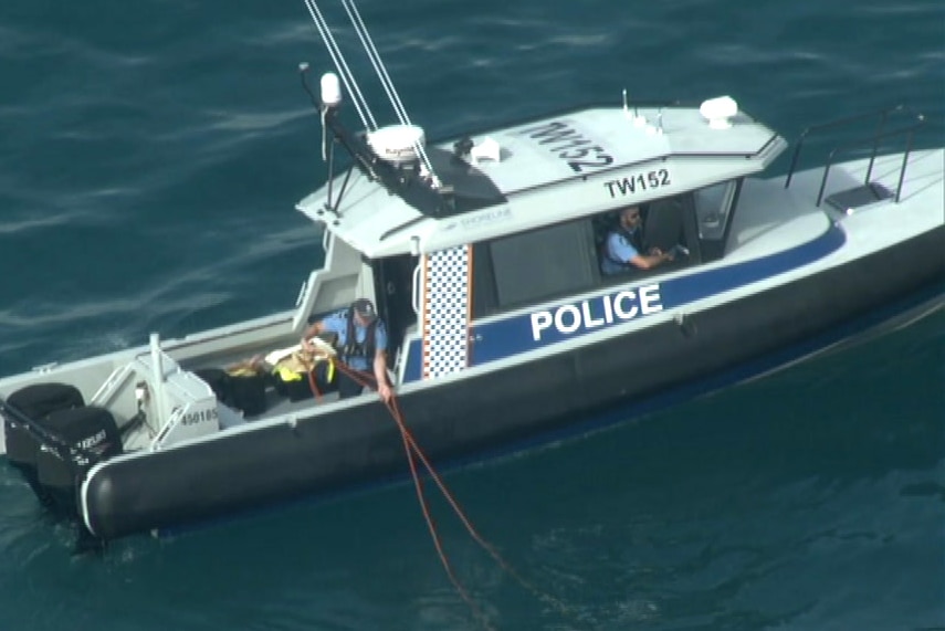 A water police boat with an officer on board pulling a rope from the water.