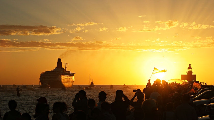 A cruise ship being watched by hordes of onlookers in the lambent light of sunset.