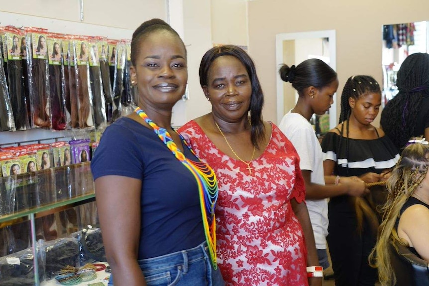 Christine and Jean Kute stand proudly in their African hair salon as clients have their hair braided in the background.