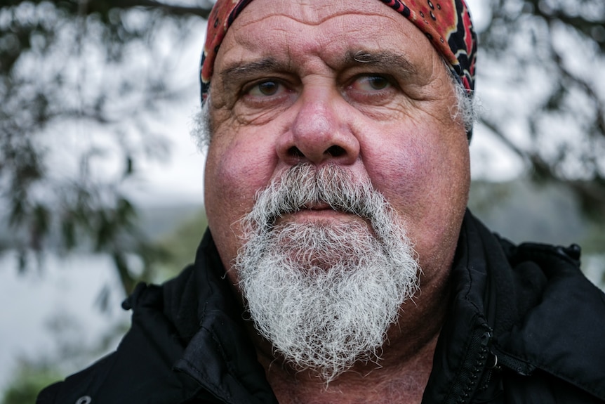 Close up of bearded man with determined expression, lake and trees in background