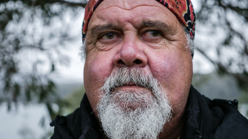 Close up of bearded man with determined expression, lake and trees in background