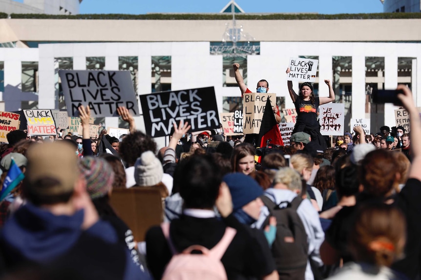 Placards saying Black Lives Matter are seen held up outside Parliament House by a large group of people.