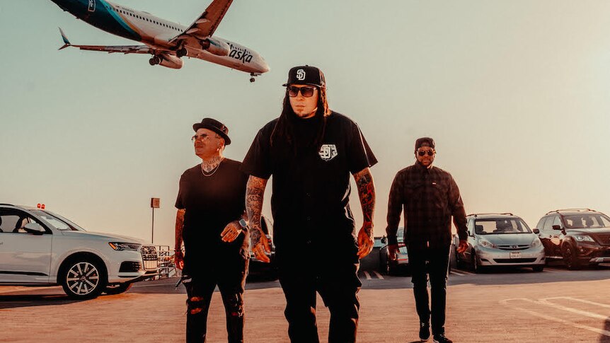 Press photo of P.O.D. with three members dressed in black in an airport carpark 