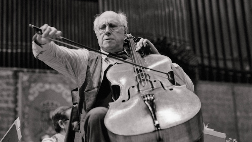 A view looking up towards a cellist in performance. His bow arm is extended and his expression is serious.