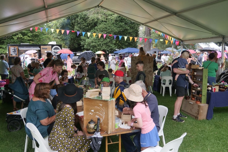 A gathering of people inside a festival tent who are sitting at tables and working with craft items