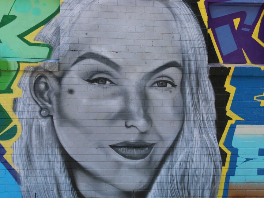 The face that is grey and white has been painted onto the wall amid other paintings.