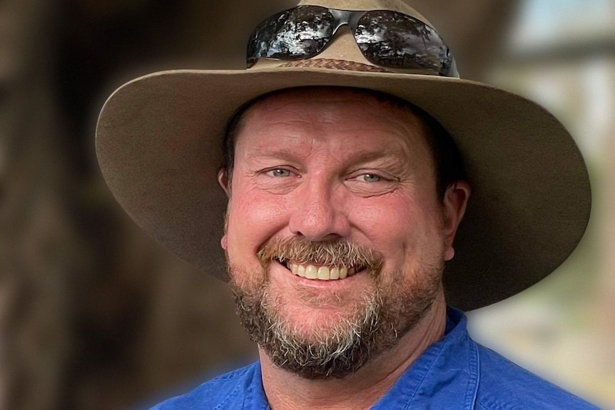 man wearing blue shirt and akubra, with black sunglasses on top