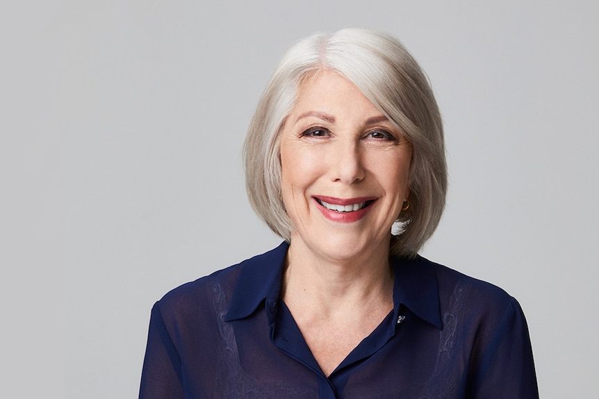 A woman with grey hair looks and smiles at the camera