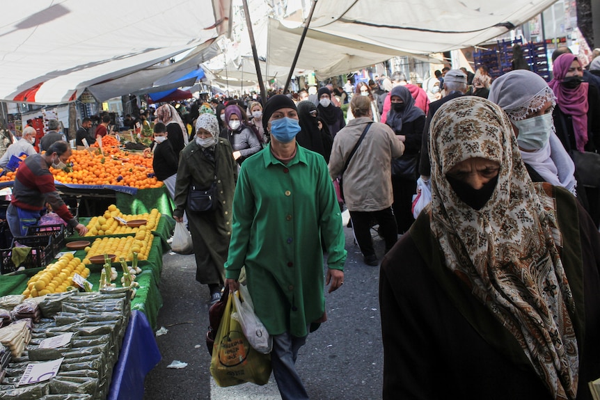 Menschen, die Gesichtsmasken tragen, kaufen auf einem Markt für frische Lebensmittel ein.