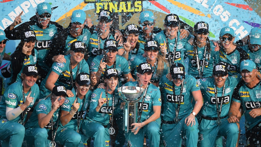 Brisbane Heat players hold the WBBL championship trophy, as they celebrate on a podium after beating Adelaide Strikers.