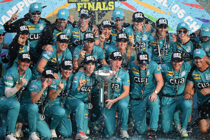 Brisbane Heat players hold the WBBL championship trophy, as they celebrate on a podium after beating Adelaide Strikers.