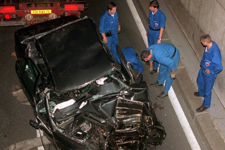 Emergency services inspect a black crumpled car