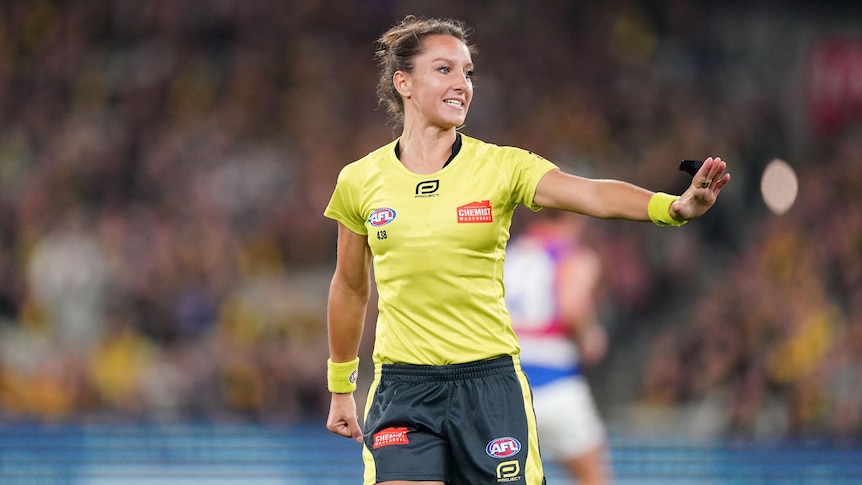 A female AFL field umpire has her left hand held to her side during a match.