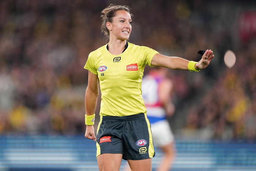 A female AFL field umpire has her left hand held to her side during a match.