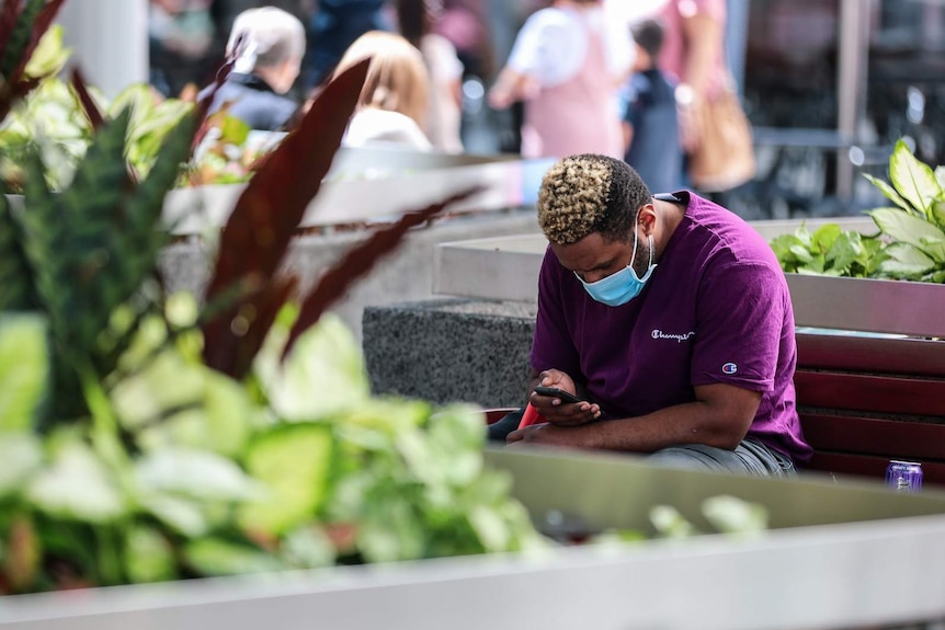 A man wearing a face mask sat down and looking at his phone