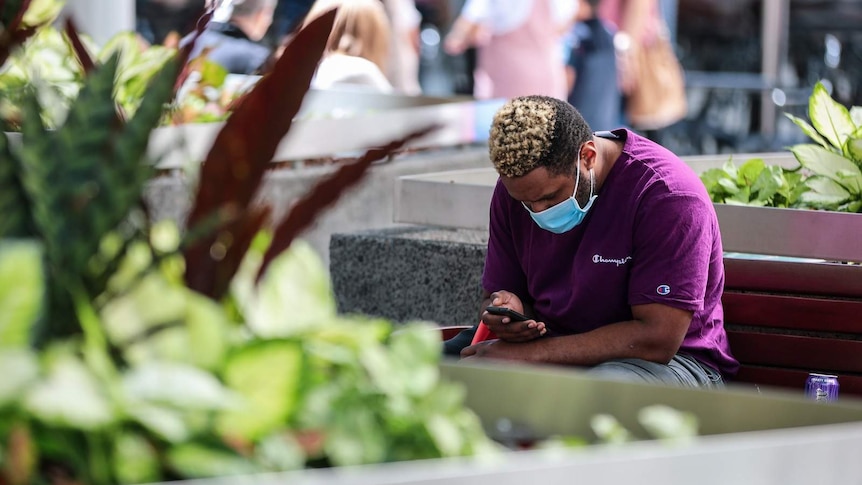 A man wearing a face mask sat down and looking at his phone