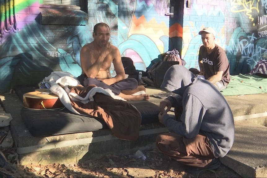 Homeless people in front of a graffitied wall.