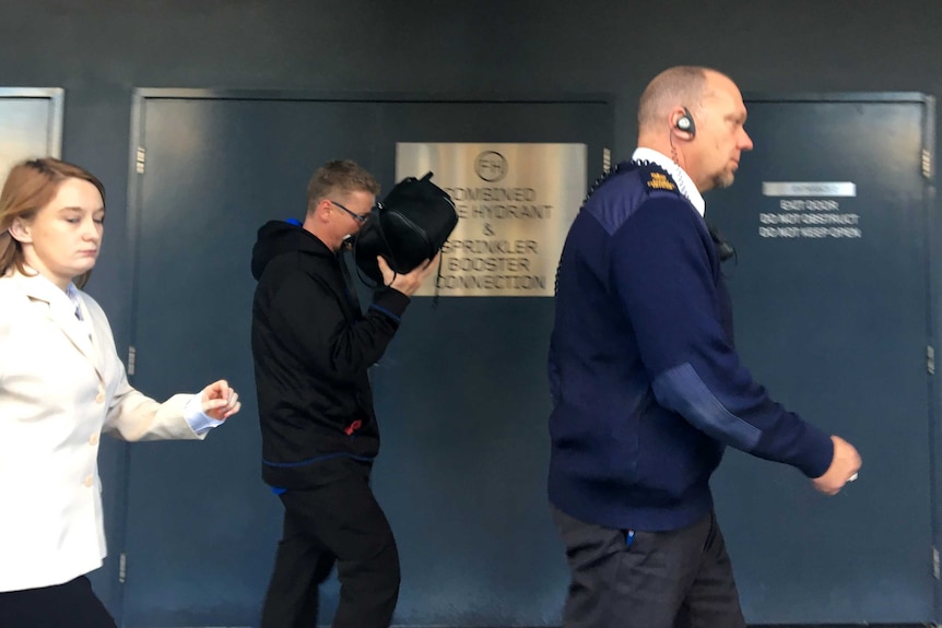 Darren Blak walking outside court while trying to hide his face with a bag.