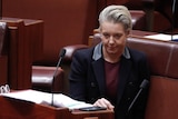 McKenzie sitting at her desk in the senate, wearing a dark jacket.