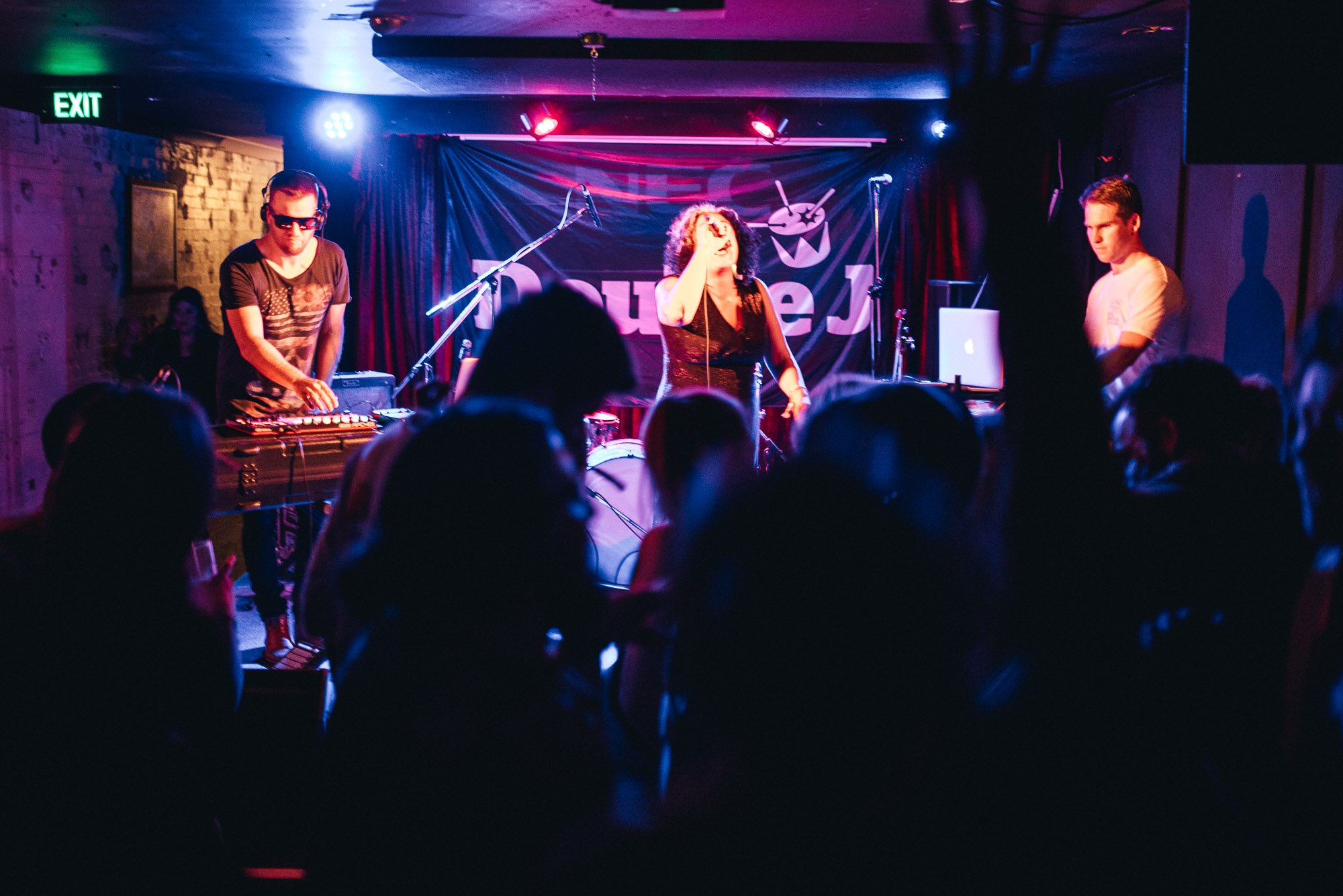 A woman sings onstage with a band and a Double J banner behind.
