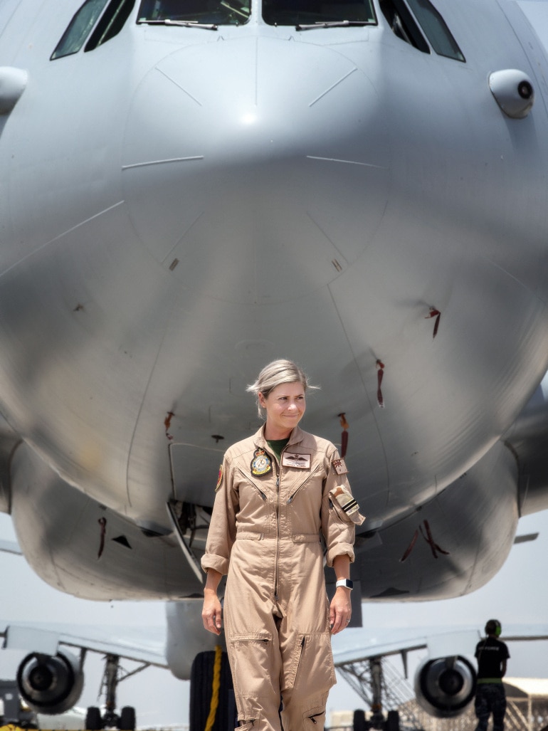 Woman in RAAF overalls walking under the nose cone of a gigantic military plane