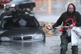 A man wearing a black jumper wades through ankle-deep flood waters after gathering items from his BMW car submerged in floods.