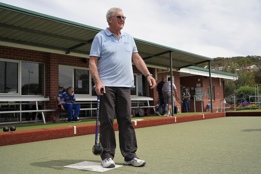 A man in a polo shirt playing bowls with the aid of an arm-extending device.
