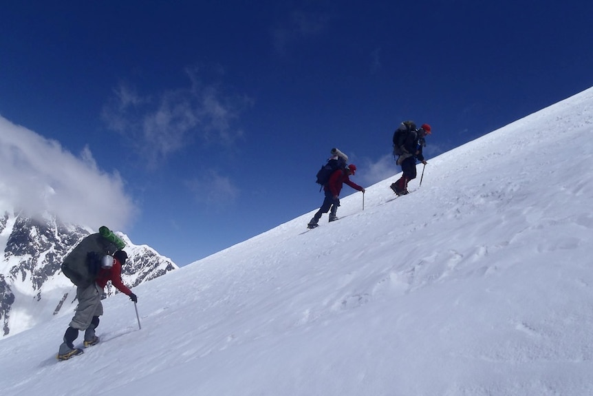 Three climbers march up the icy slope of Noshaq
