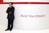 A middle-aged Chinese man in a black suit standing next to a sign that says 'Build Your Dreams'