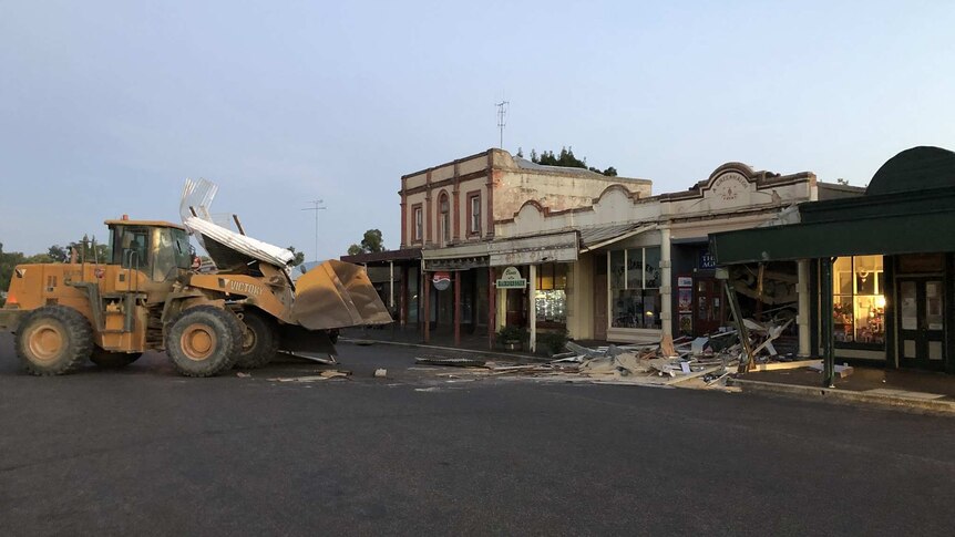 A front-end loader stands in front of a shopfront that has been smashed in.