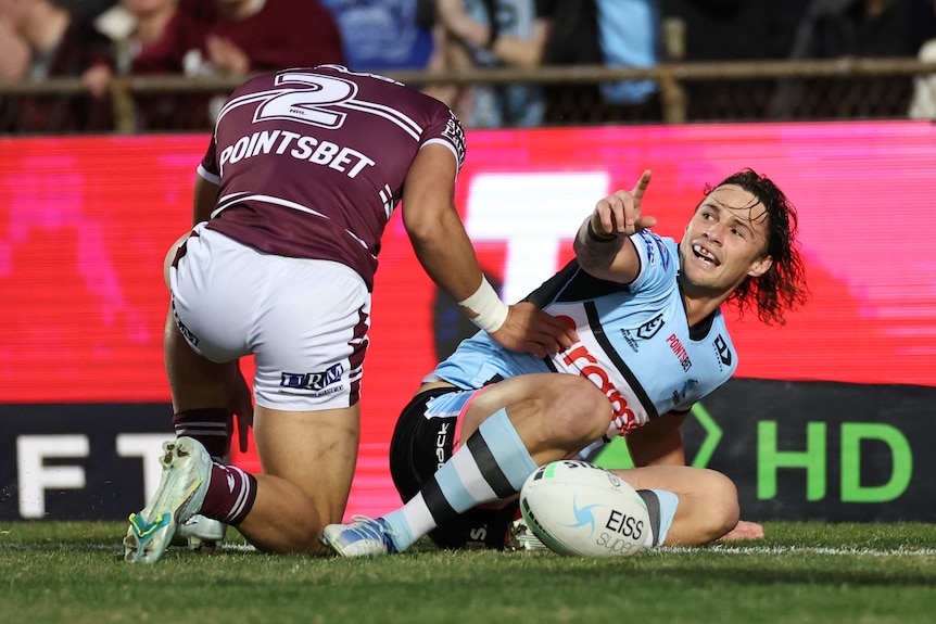 Cronulla Sharks' Nicho Hynes puts a finger in the air to celebrate a try with a Manly player nearby.