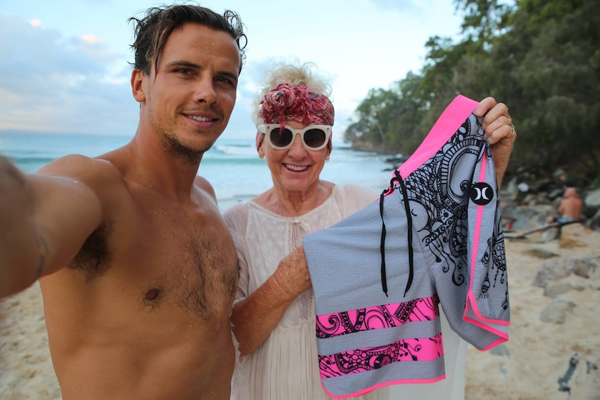 Son and mother at the beach holding up pink board shorts, smiling.
