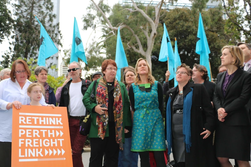 A group of protesters holding flags and a Rethink Perth Freight Link placard