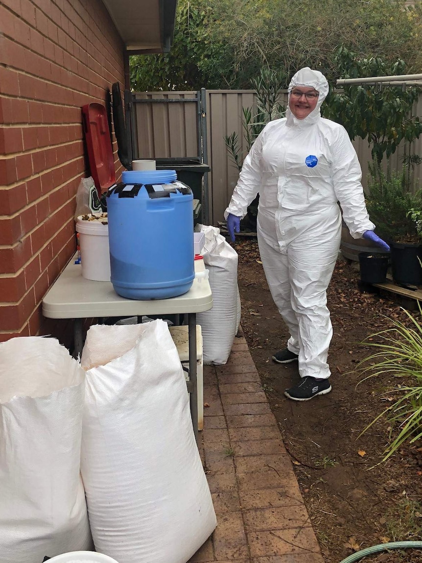 Emily Bryson stands in a protective suit next to her compost trial with white bags and a blue compost container.