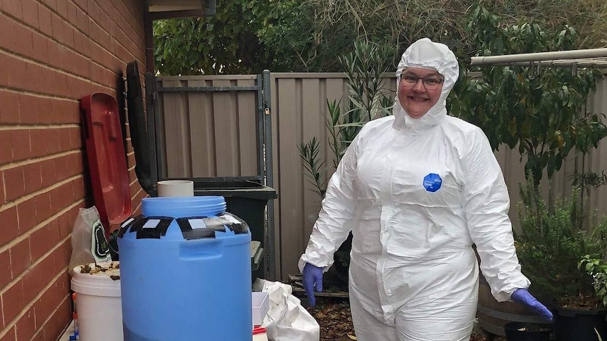 Emily Bryson stands in a protective suit next to her compost trial with white bags and a blue compost container.