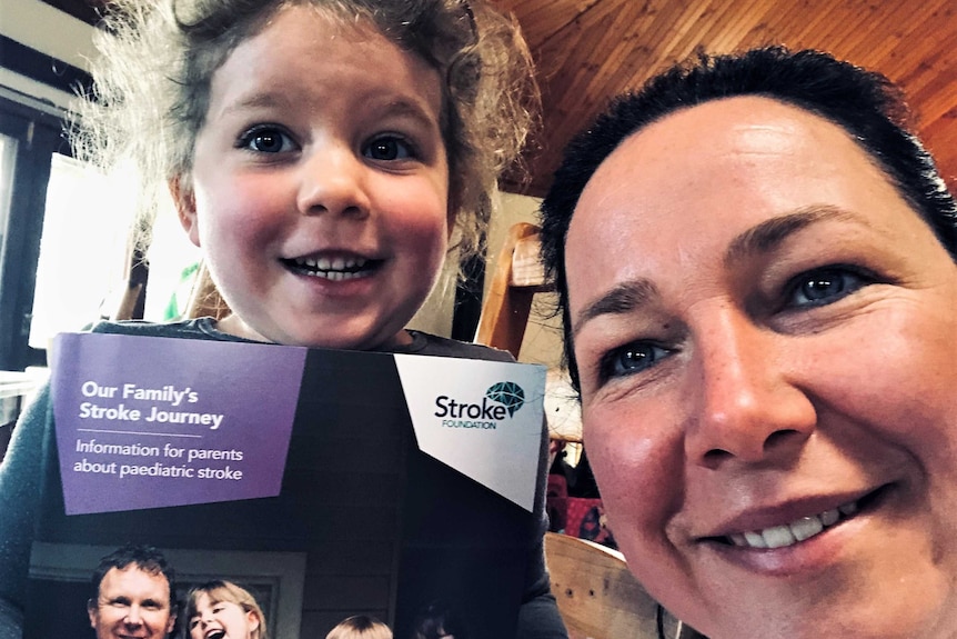 A woman and her young daughter posing for a selfie, with the daughter holding a booklet with stroke terminology written on it.