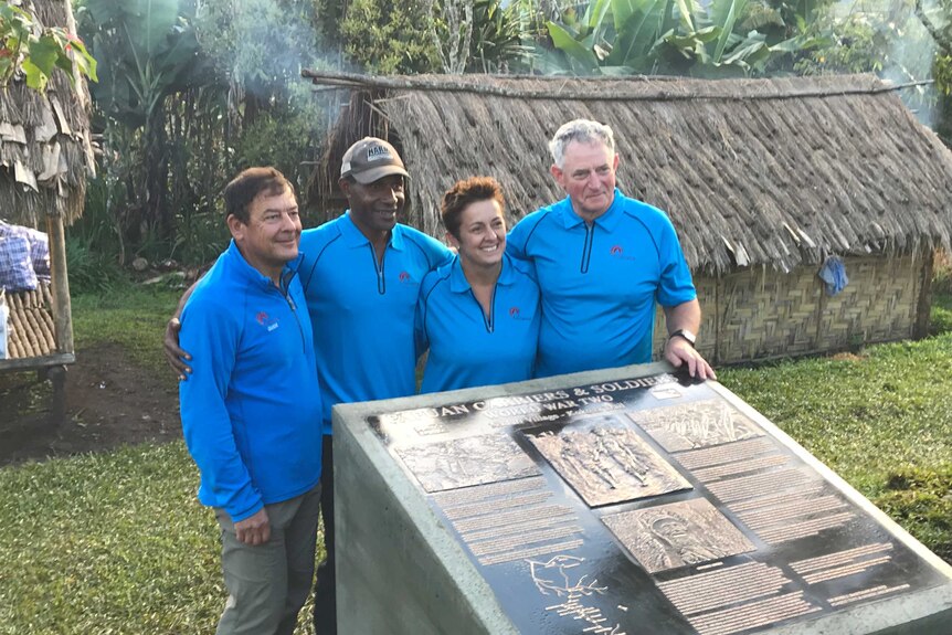 Four people dressed in blue t-shirts next to a plaque.