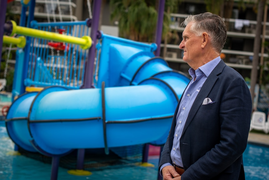 A man in a jacket and shirt watches over a water park play area.