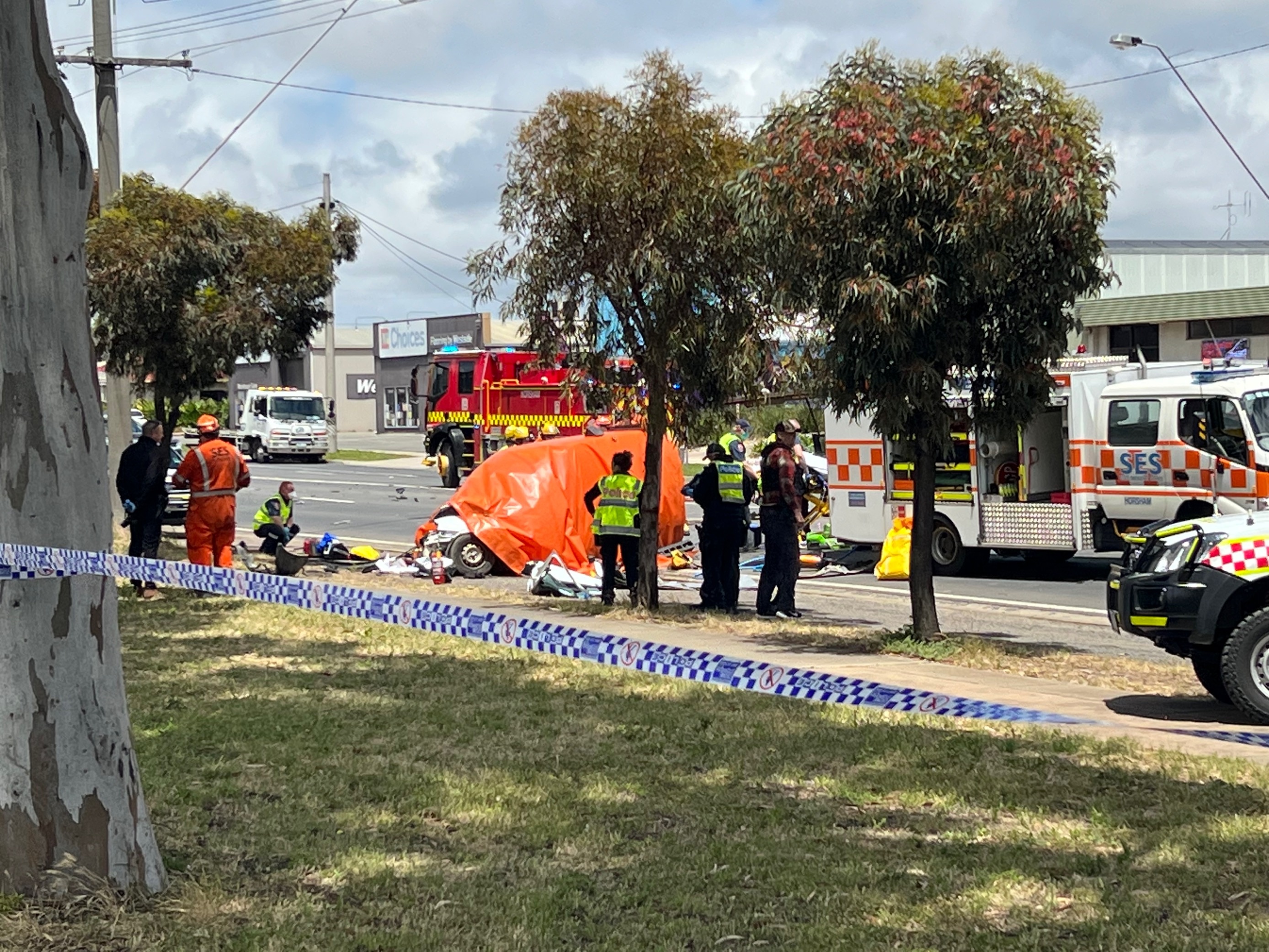 SES, Police and CFA vehicles and personnel attend to a car crash on a sunny day. One car has an orange tarpaulin on it.