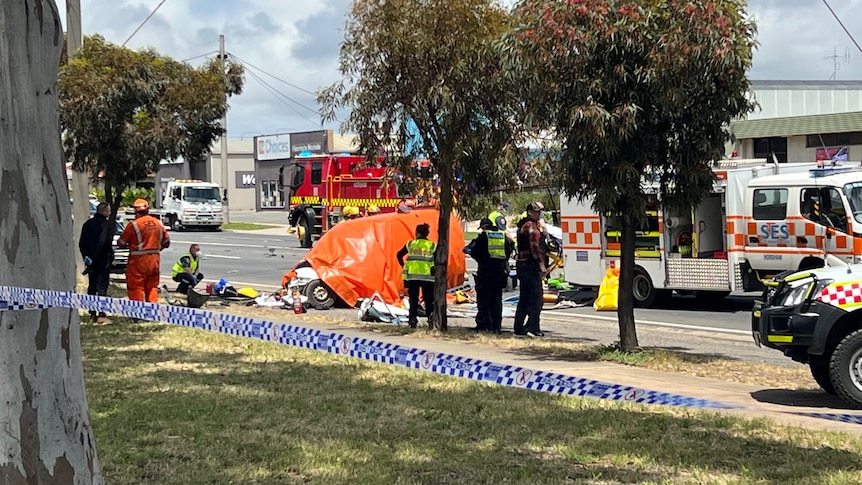 SES, Police and CFA vehicles and personnel attend to a car crash on a sunny day. One car has an orange tarpaulin on it.