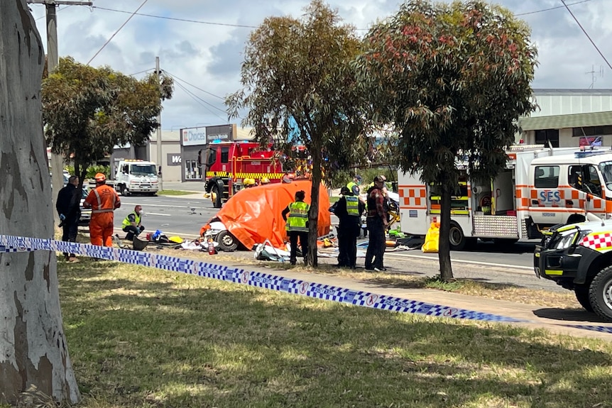 SES, Police and CFA vehicles and personnel attend to a car crash on a sunny day. One car has an orange tarpaulin on it.