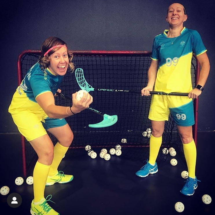 Two women smile for the camera while in floorball uniform