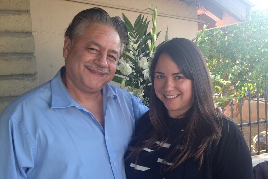 An older man with his arm around a young woman outside a house