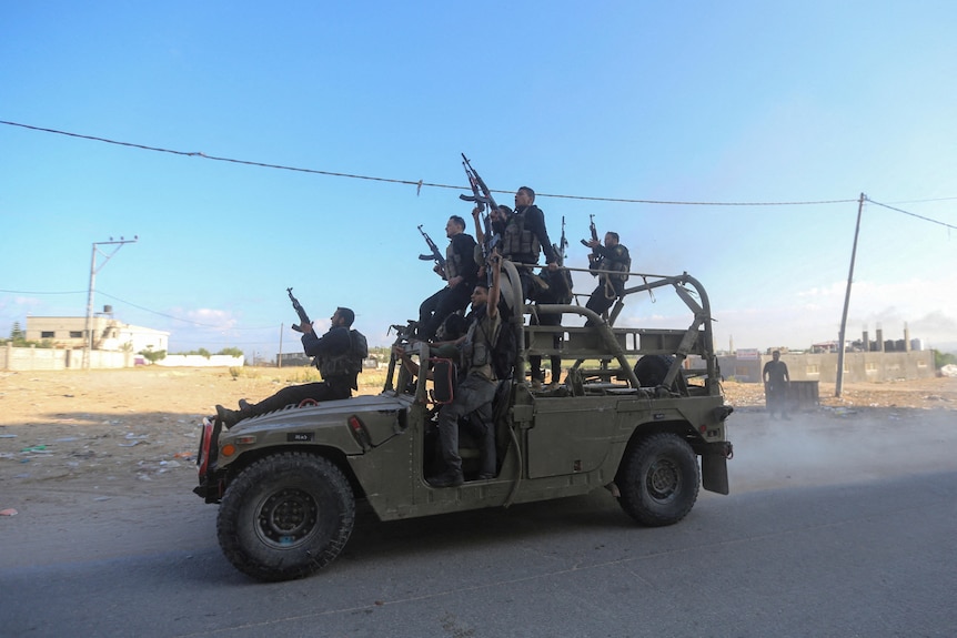People stand holding machine guns on the back of a military vehicle 