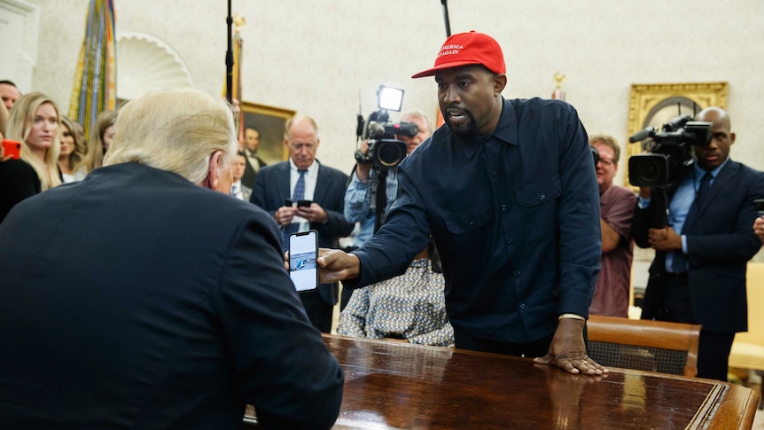 Rapper Kanye West shows President Donald Trump a photograph on his phone of a hydrogen plane in the Oval Office.