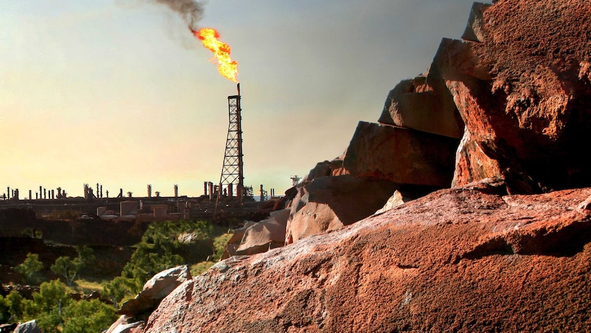 Aboriginal rock art in the Pilbara with a flame from a mining industry development in the background.